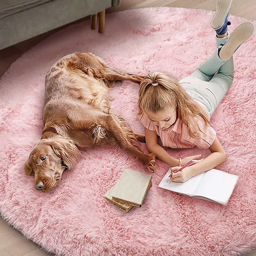 Fillette qui dessine sur un tapis rond rose poil long avec un cocker à côté