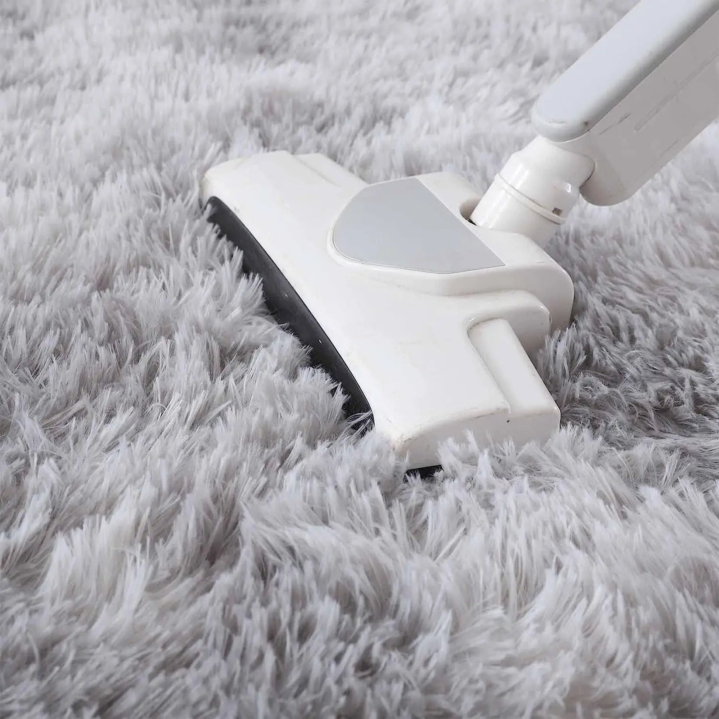 Aspirateur balai passant sur un tapis rond gris clair à poil long