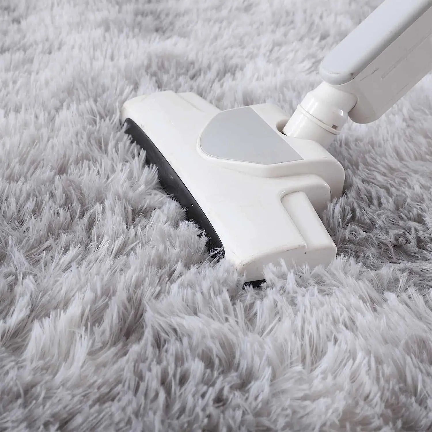 Aspirateur balai passant sur un tapis rond gris clair à poil long