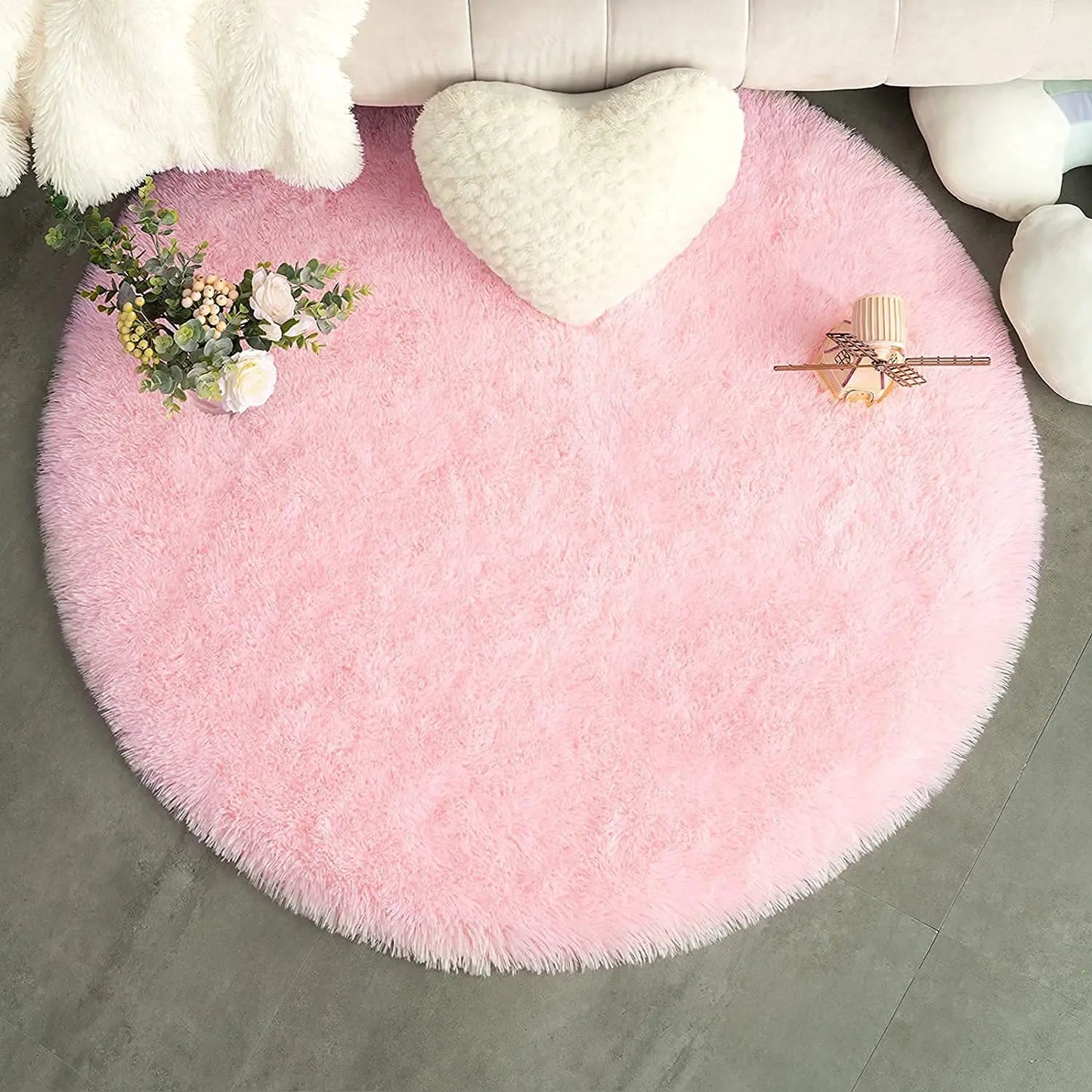 Tapis rond rose poil long avec coussin cœur blanc et bouquet de roses sur sol gris