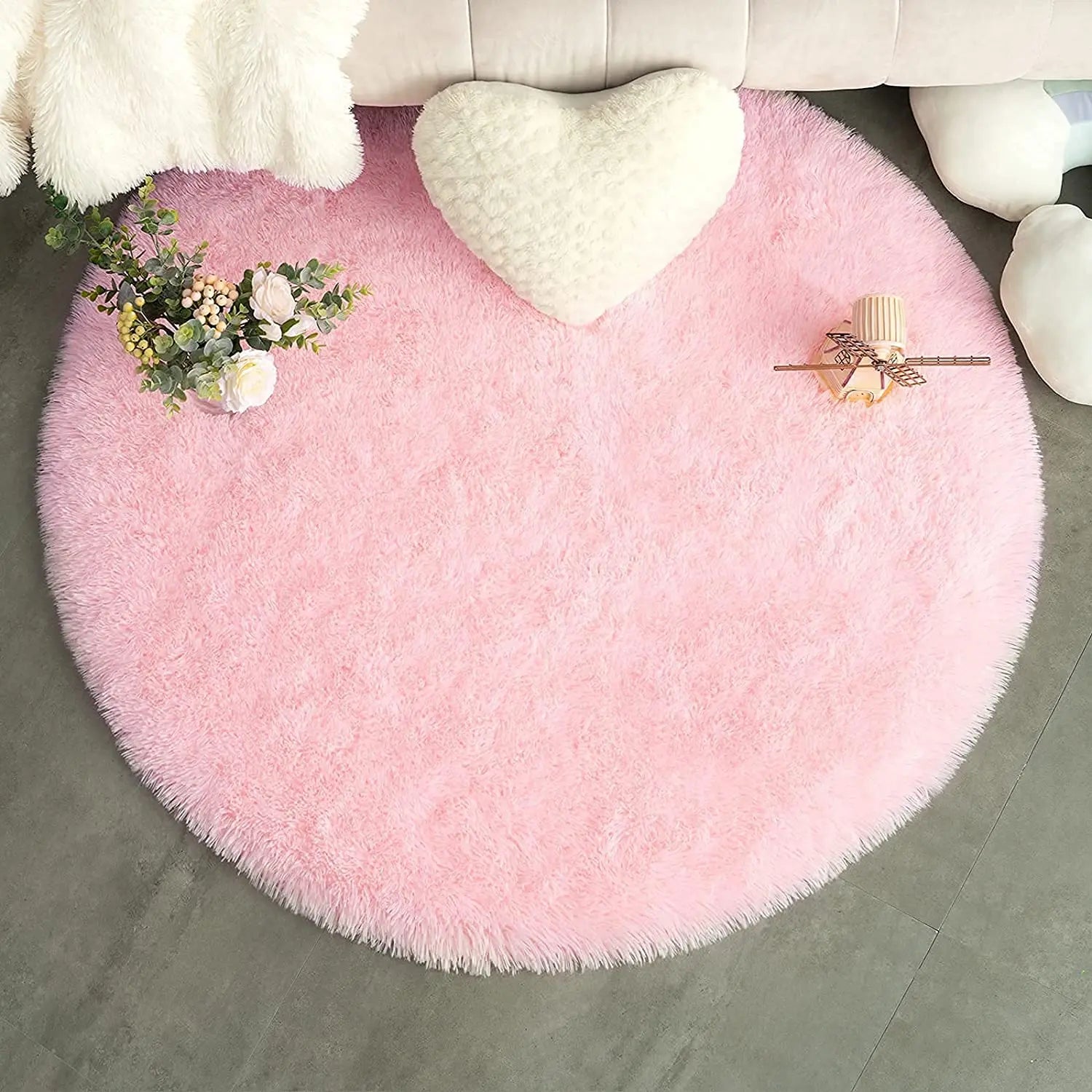 Tapis rond rose poil long avec coussin cœur blanc et bouquet de roses sur sol gris