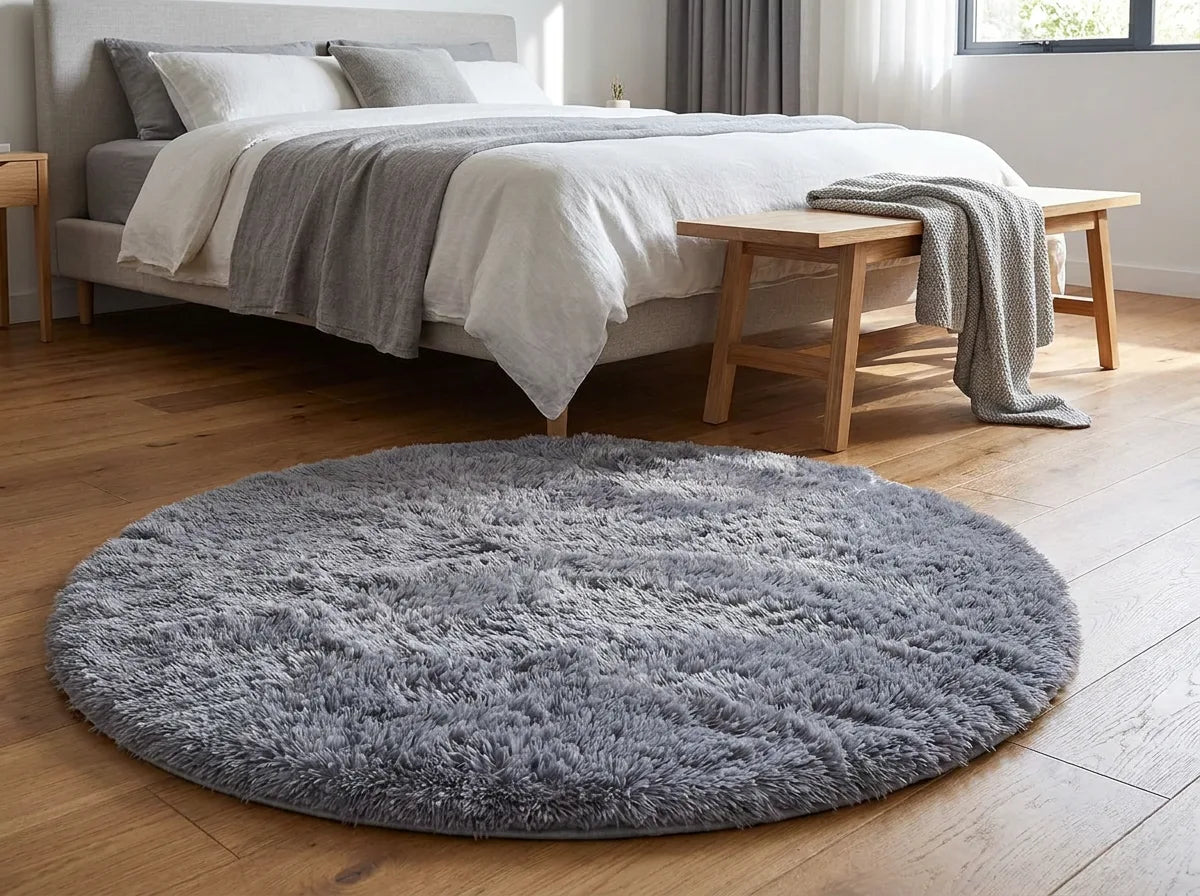 Tapis rond chambre moelleux gris au pied du lit, devant un banc en bois clair