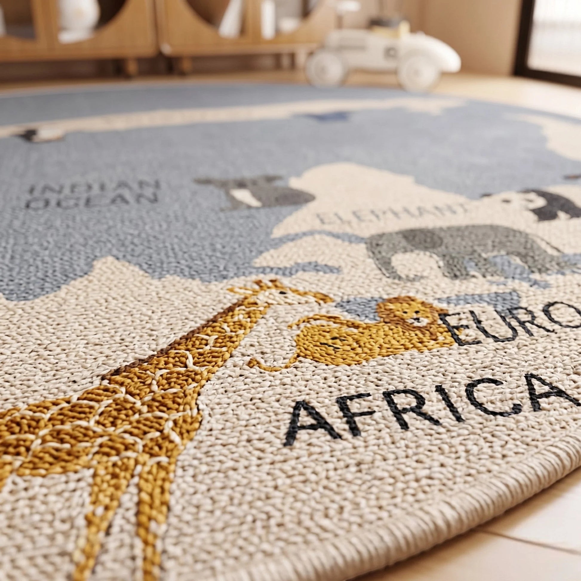 Vue rapprochée du tapis rond enfant carte du monde animaux gris posé sur un parquet, montrant la finesse du tissage et le contraste continents-océan