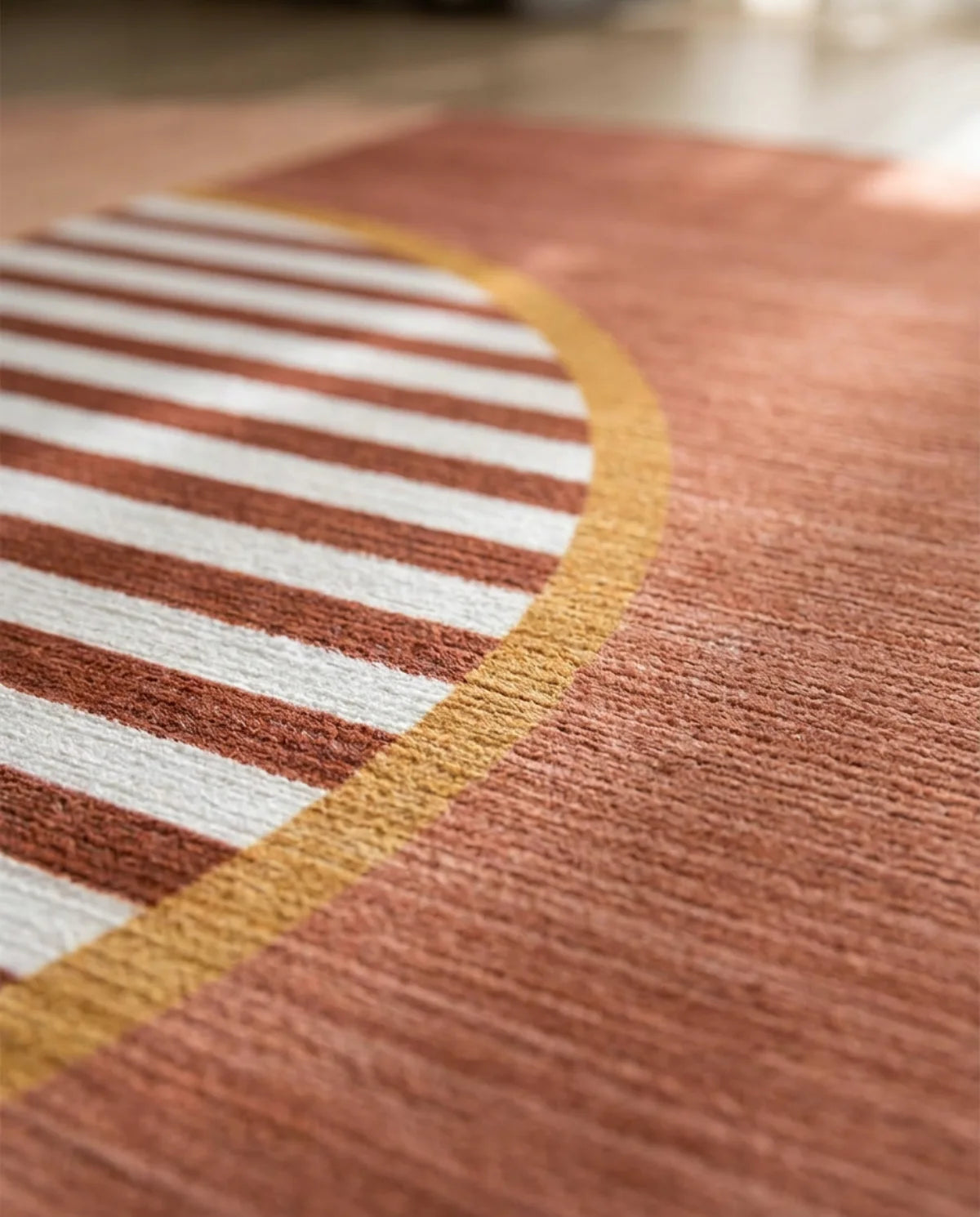 Détail du demi-cercle rayé et du liseré ocre du tapis rond lavable terracotta
