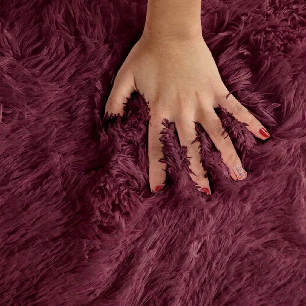 Macro de la peluche du tapis rond salle de bain moelleux rouge bordeaux, main posée sur les fibres longues