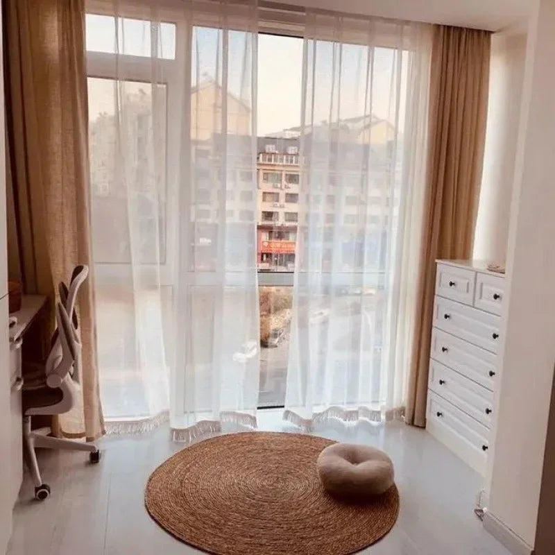 Variante spirale tressée : tapis rond rotin devant une baie vitrée voilée avec pouf rond et coin bureau